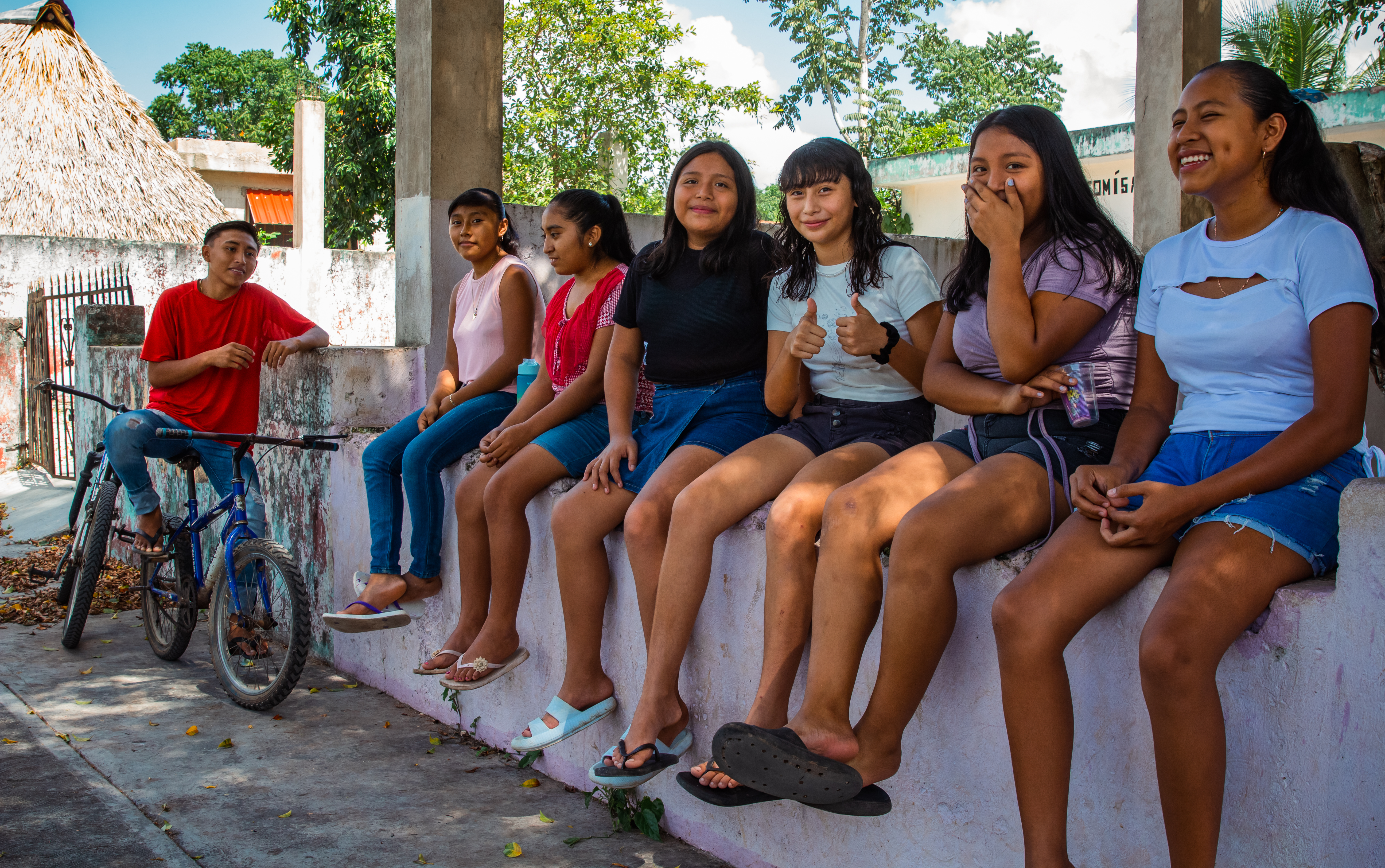 Seis niñas sentadas en una barda mirando a la cámara