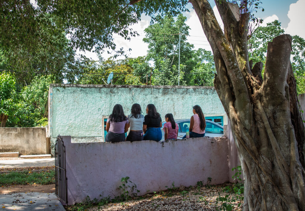 Cinco niñas sentadas de espalda sobre una barda durante una actividad de Save the Children