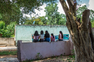 Cinco niñas sentadas de espalda sobre una barda durante una actividad de Save the Children