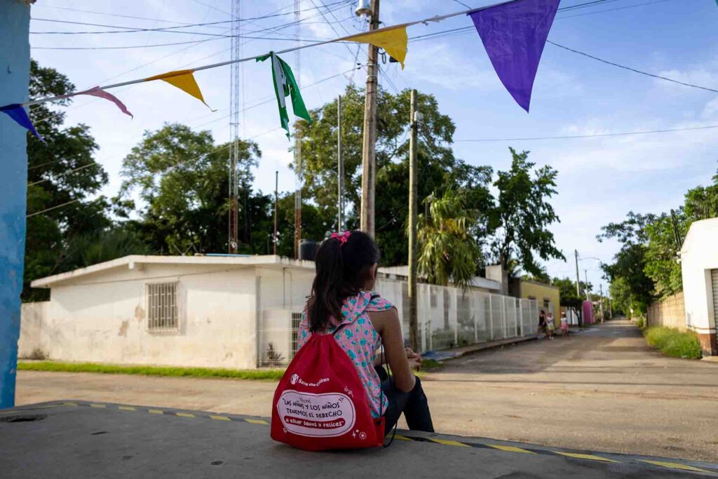Nina sentada en la acera con mochila de Save the Children
