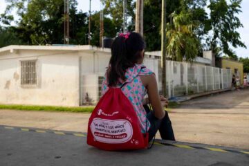 Nina sentada en la acera con mochila de Save the Children