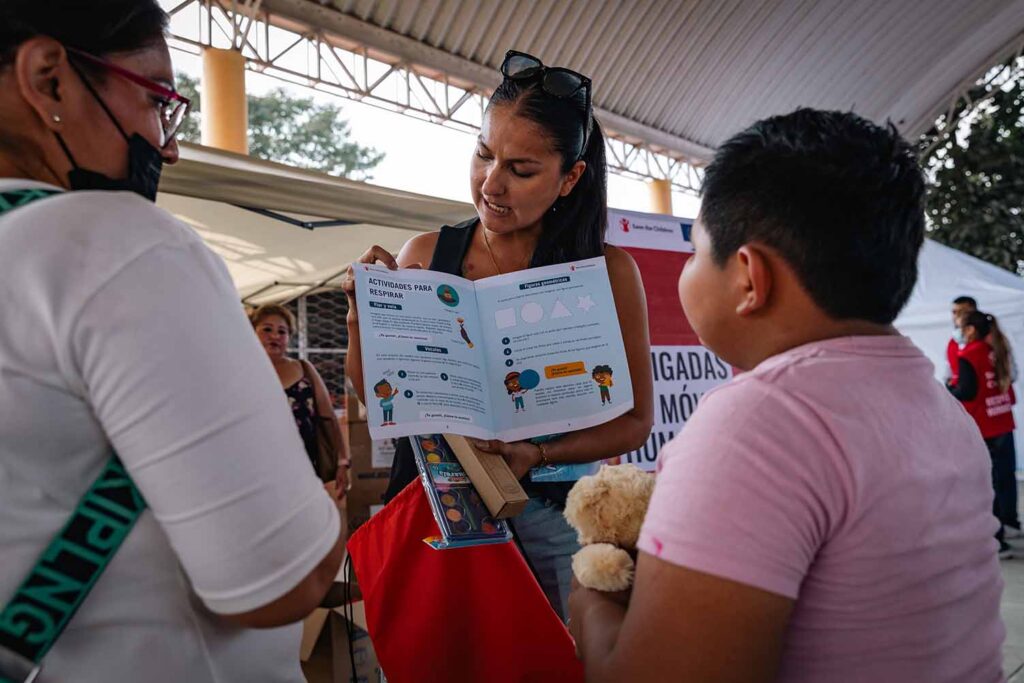 Profesora previamente entrenada en primeros auxilios psicologicos mostrando a niñas y niños qué incluye uno de los kits de SCMx